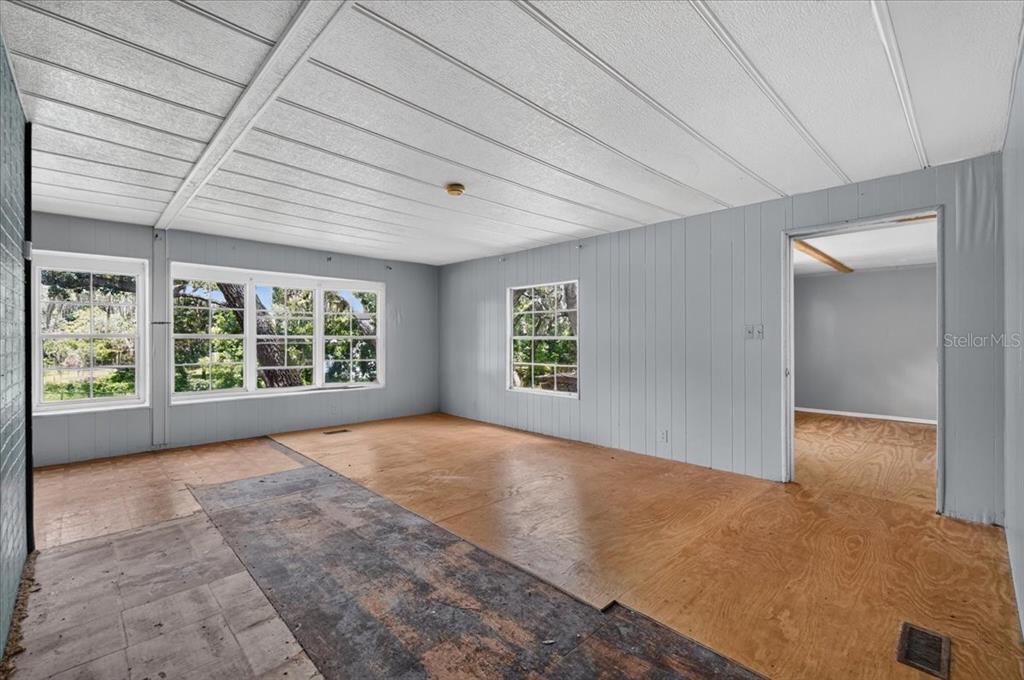 An interior room with light gray paneled walls, exposed plywood flooring, and several windows — 12489 SW 45TH TERRACE, WEBSTER, FL
