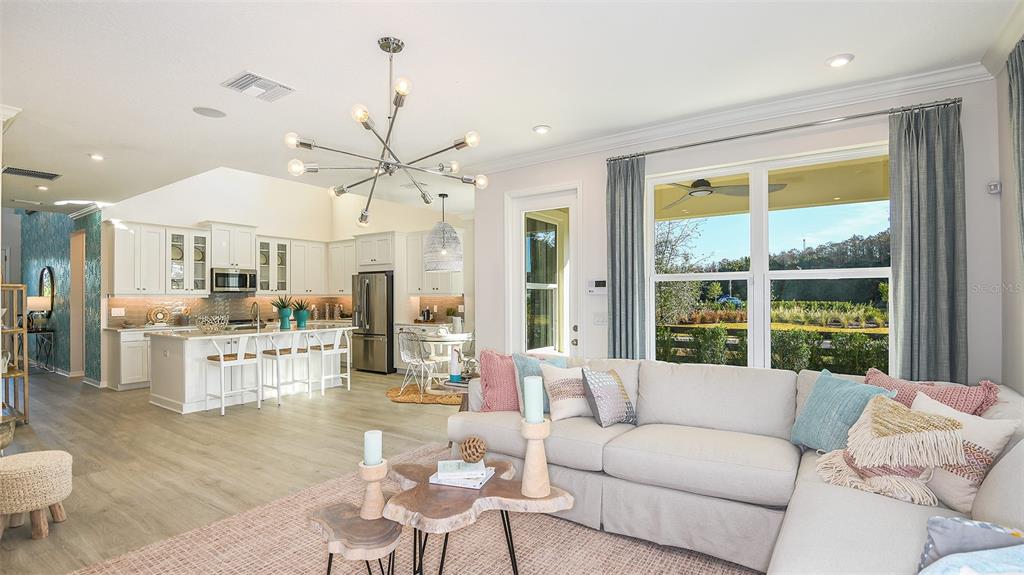 An open-concept living room and kitchen feature light wood flooring, white cabinetry, and large windows — 14736 FIELD DAISY DRIVE, WINTER GARDEN, FL