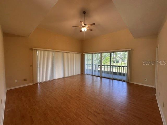An empty living room features wood-look flooring, a vaulted ceiling with a fan, and sliding doors — 35 MAGNOLIA AVENUE UNIT 35, ORMOND BEACH, FL