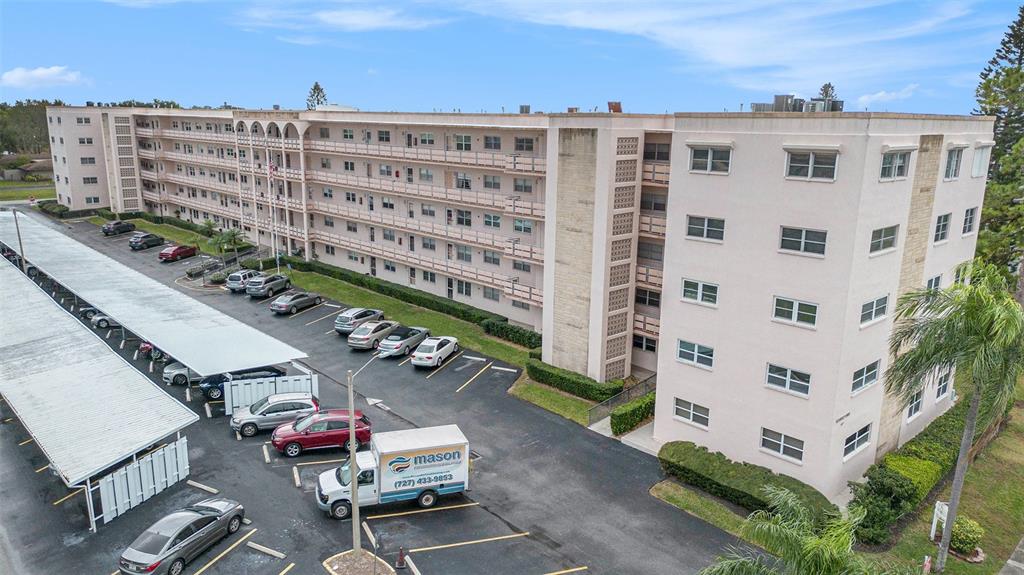 An aerial view shows a multi-story apartment building with a parking lot and covered carports — 5623 80TH STREET N UNIT 211, ST PETERSBURG, FL