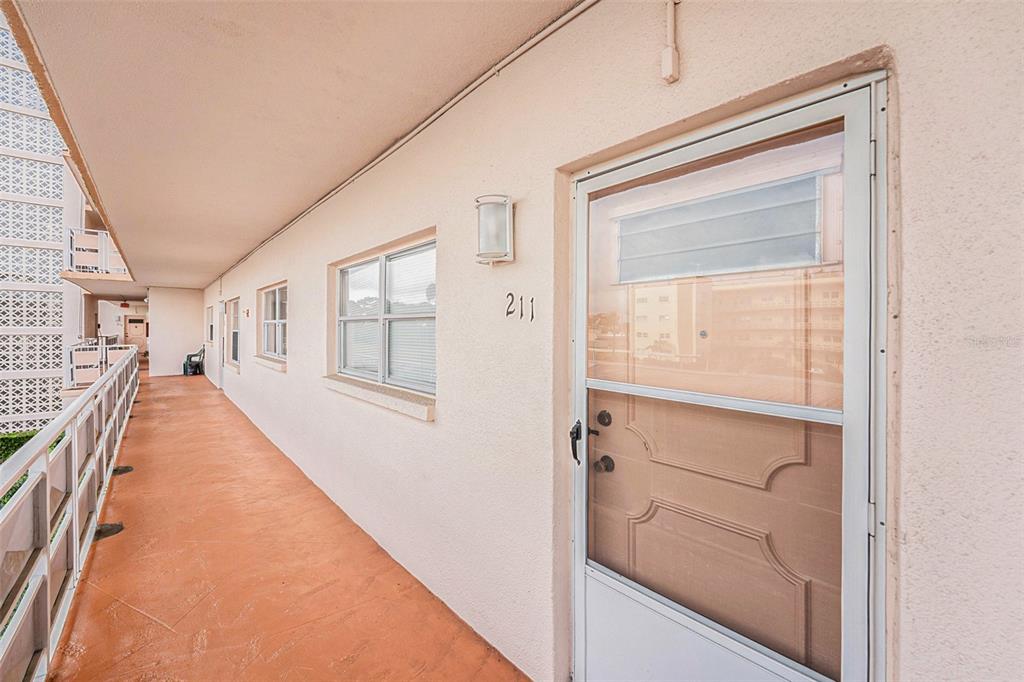 An exterior walkway with a tan wall, windows, and a door labeled 211 — 5623 80TH STREET N UNIT 211, ST PETERSBURG, FL