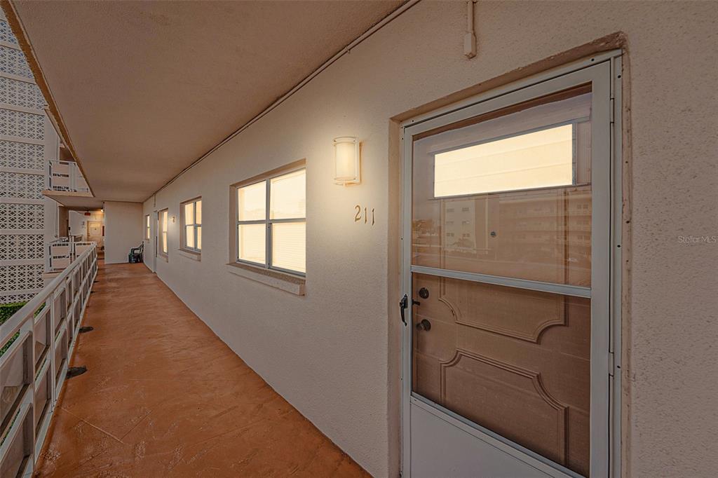 An exterior apartment hallway features a door labeled 211, windows, and a metal railing — 5623 80TH STREET N UNIT 211, ST PETERSBURG, FL