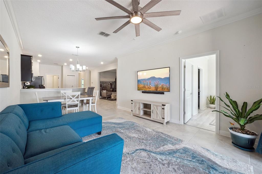 A living room features a blue sectional sofa, a wall-mounted television, and a ceiling fan — 3569 BELLAND CIRCLE UNIT C, CLERMONT, FL