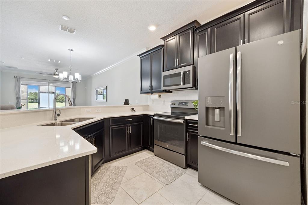 A kitchen features dark wood cabinets, stainless steel appliances, and a light-colored quartz countertop — 3569 BELLAND CIRCLE UNIT C, CLERMONT, FL