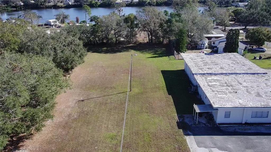 An aerial view shows a vacant grassy lot next to a white building near water — 0 6TH STREET, MULBERRY, FL