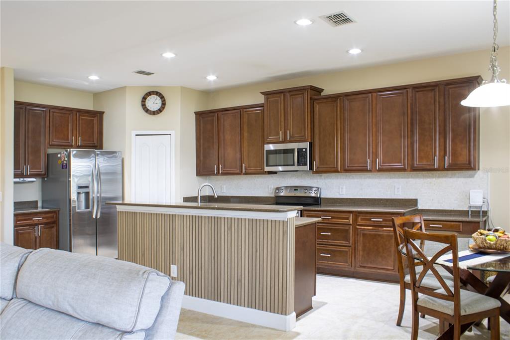 A kitchen features dark wood cabinets, stainless steel appliances, and a slatted wood kitchen island — 1112 GLENRAVEN LANE, CLERMONT, FL
