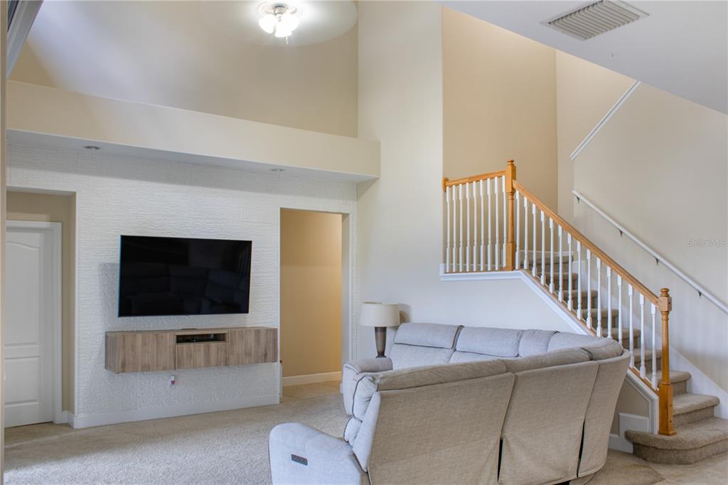 A living room features a wall-mounted television, a light-colored sectional sofa, and a staircase — 1112 GLENRAVEN LANE, CLERMONT, FL
