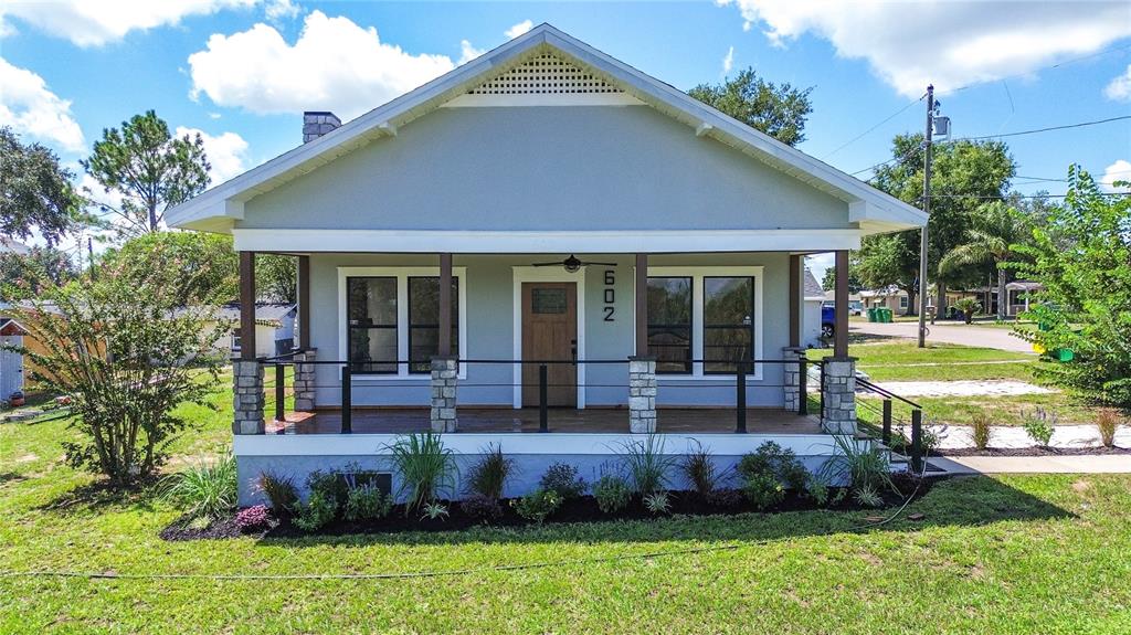 A light gray bungalow features a covered front porch with stone pillars and wood flooring — 602 EDMUND AVENUE, DUNDEE, FL