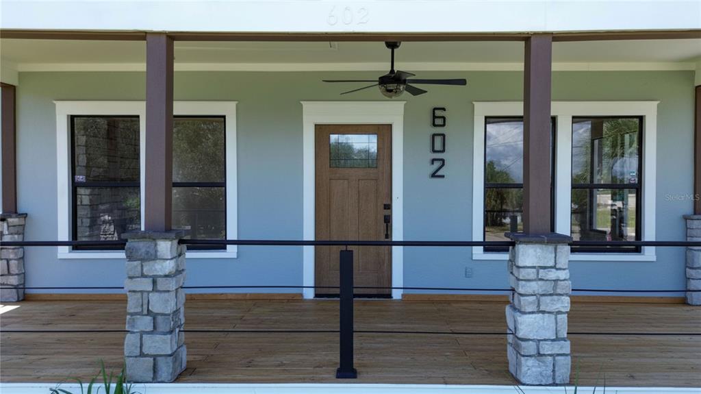 A covered front porch features a wooden door, stone-based columns, and a ceiling fan — 602 EDMUND AVENUE, DUNDEE, FL