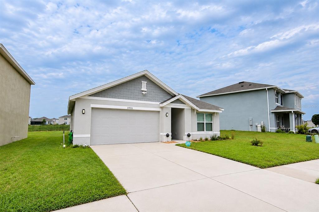 A single-story suburban house with a gray garage, light siding, and a concrete driveway — 37093 SHARKS EYE LANE, ZEPHYRHILLS, FL