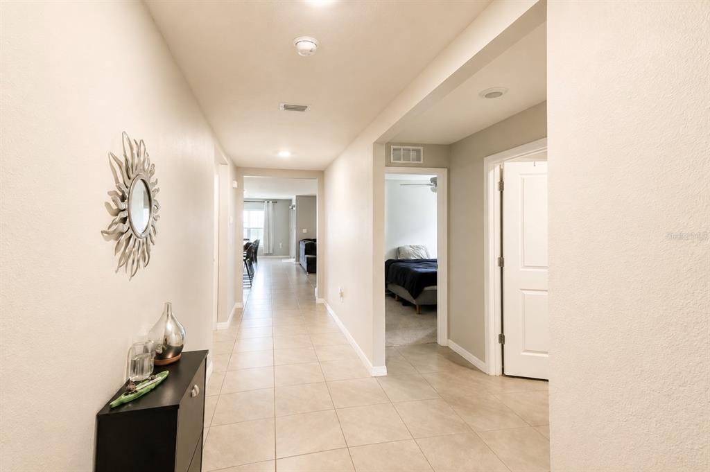 A tiled hallway leads to a living area and a bedroom with a sunburst mirror — 37093 SHARKS EYE LANE, ZEPHYRHILLS, FL