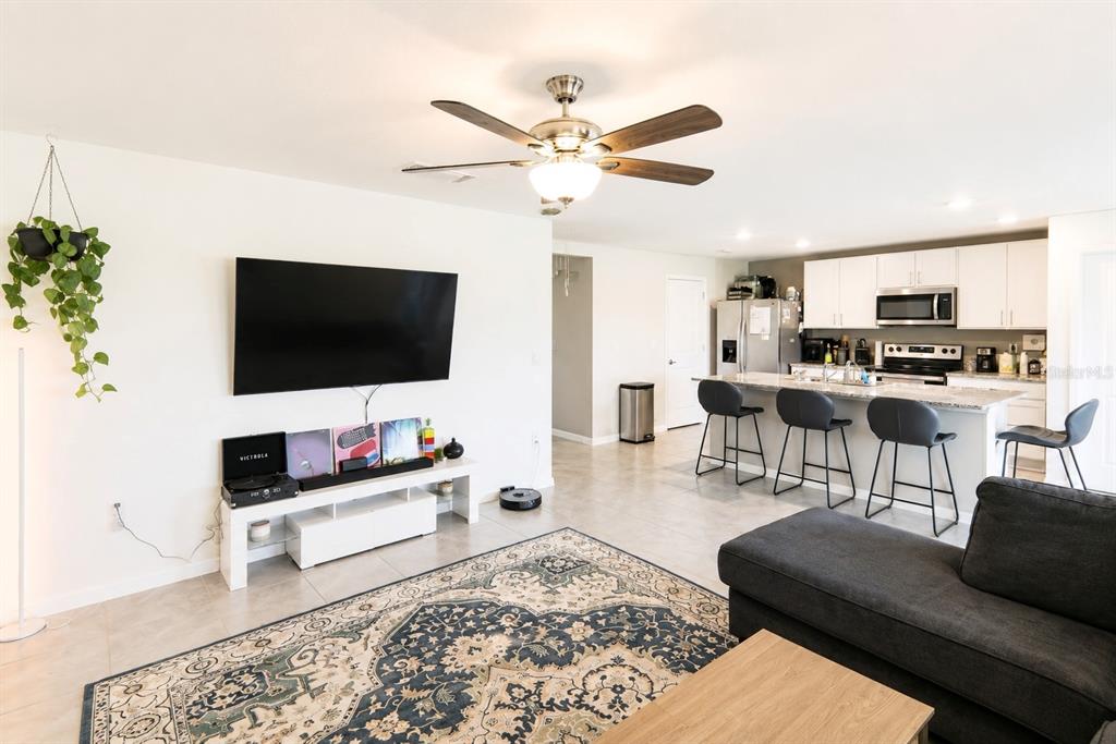 A living room with a television, media console, and area rug opens into a kitchen — 37093 SHARKS EYE LANE, ZEPHYRHILLS, FL