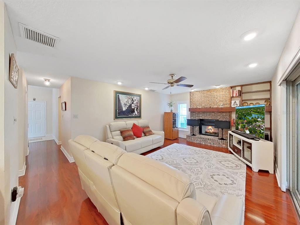A living room features a brick fireplace, built-in shelving, hardwood floors, and two leather sofas — 1367 CORNER OAKS DRIVE, BRANDON, FL