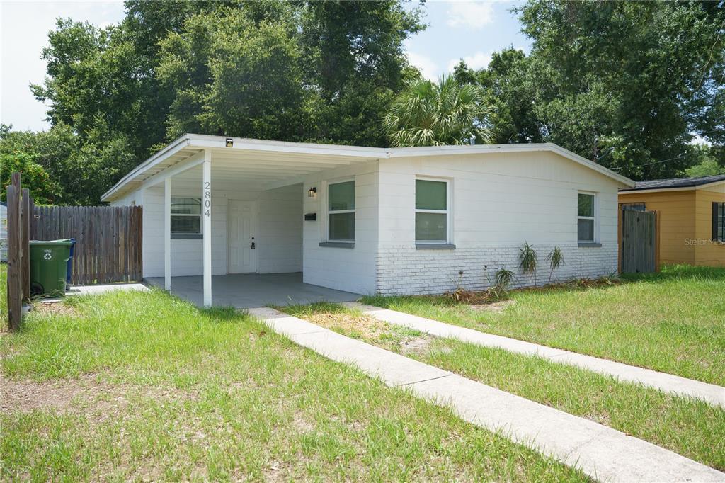 A single-story white house with a carport and a concrete driveway sits on a lawn — 2804 N 33RD STREET, TAMPA, FL