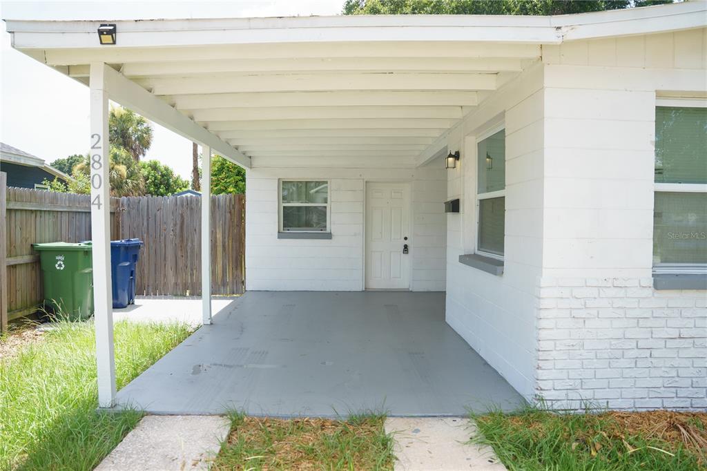 A white house exterior features a covered concrete carport and a front entrance door — 2804 N 33RD STREET, TAMPA, FL