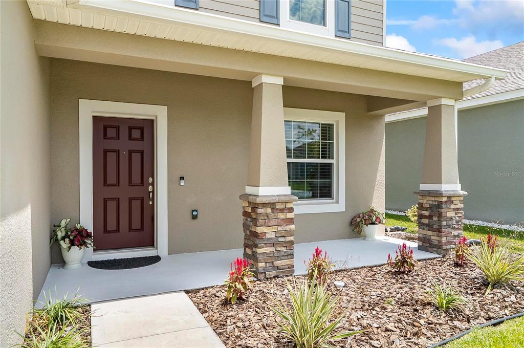 A covered front porch features a dark red door, stone-based columns, and a landscaped garden — 40 OAKLEAF WAY, PALM COAST, FL
