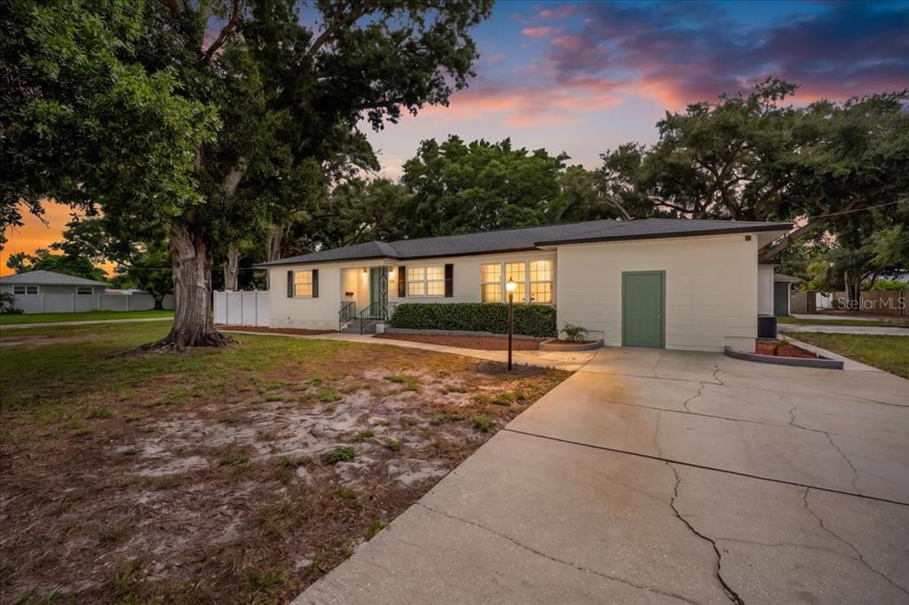 A single-story house with a concrete driveway, green door, and large trees at sunset — 125 61ST STREET N, ST PETERSBURG, FL