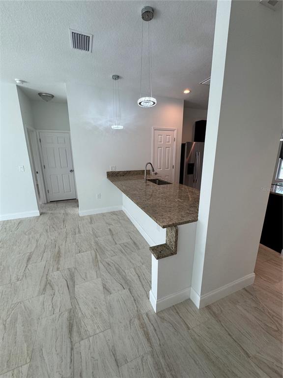 A kitchen features a granite breakfast bar, pendant lighting, and light-colored wood-look tile flooring — 2452 AINSWORTH AVENUE, DELTONA, FL