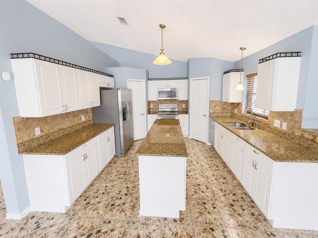 A kitchen features white cabinets, granite countertops, a central island, and speckled tile flooring — 309 ALEGRIANO COURT, KISSIMMEE, FL
