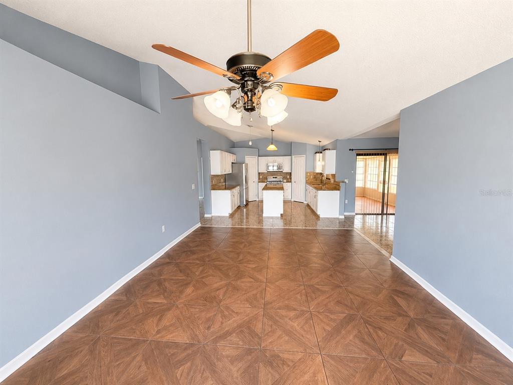 A spacious room with blue walls, tile flooring, and a ceiling fan leads to a kitchen — 309 ALEGRIANO COURT, KISSIMMEE, FL