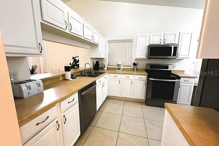 A kitchen features white cabinets, light countertops, a stainless steel dishwasher, and a black range — 3129 BEAR PATH, KISSIMMEE, FL