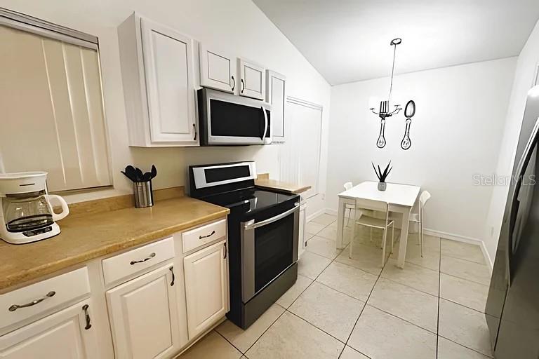 A kitchen features white cabinets, stainless steel appliances, a tan countertop, and a dining area — 3129 BEAR PATH, KISSIMMEE, FL