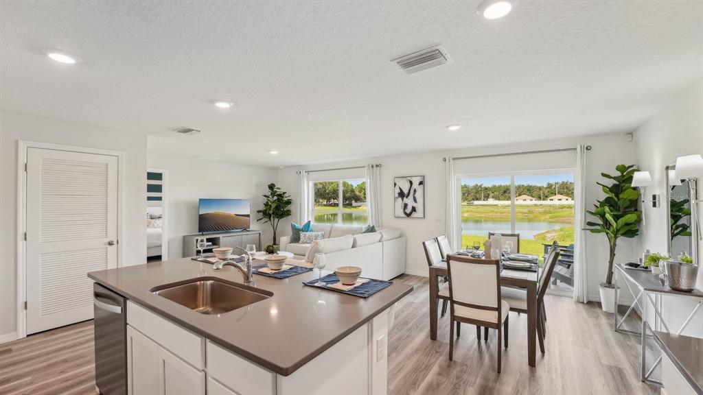 A kitchen island with a sink overlooks an open-concept living and dining area with lake views — 9806 SE 161ST LANE ROAD, SUMMERFIELD, FL