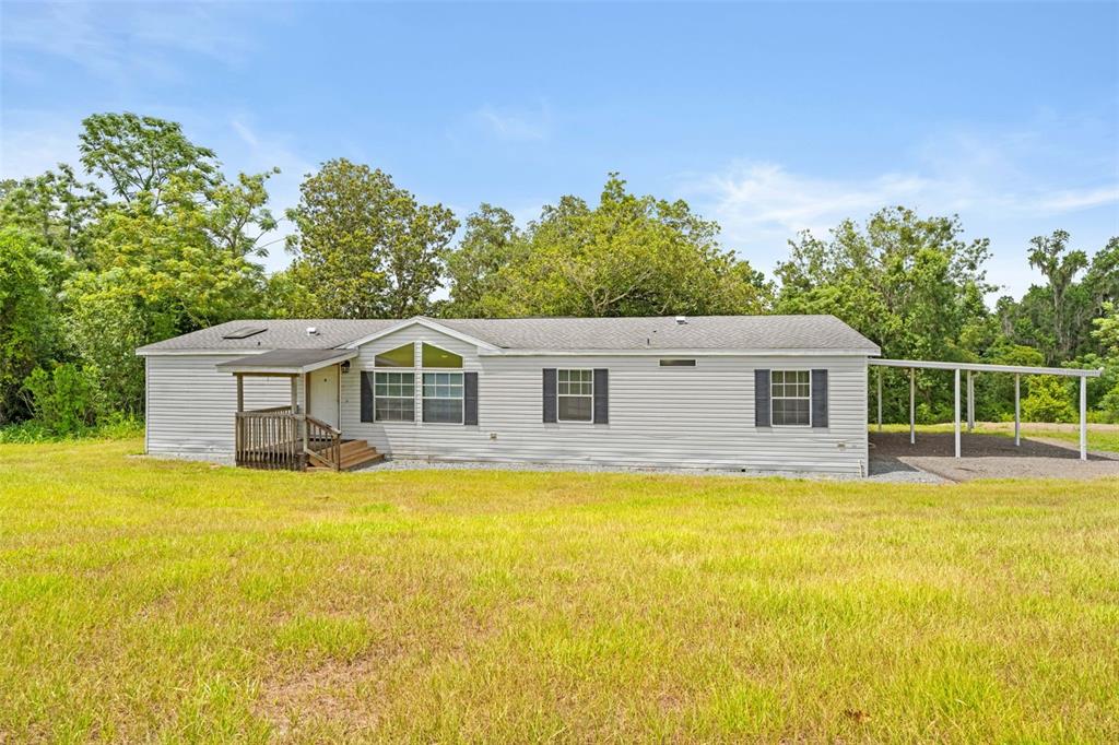 A single-story manufactured home with light siding, a small front porch, and a metal carport — 33320 LARKIN ROAD, DADE CITY, FL