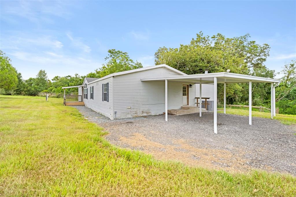 A light-colored manufactured home features a gravel driveway, a metal carport, and a wooden deck — 33320 LARKIN ROAD, DADE CITY, FL