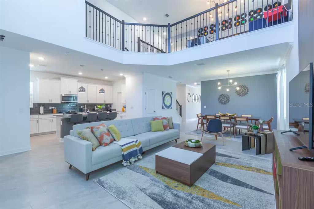 An open-concept living room and kitchen with high ceilings, a loft balcony, and modern furniture — 2924 PROTAGONIST STREET, KISSIMMEE, FL