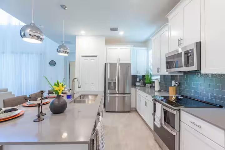 A modern kitchen features white cabinets, stainless steel appliances, and a large gray island countertop — 2924 PROTAGONIST STREET, KISSIMMEE, FL