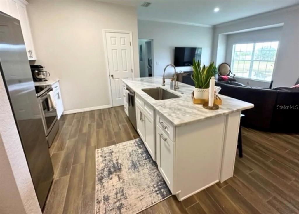 A kitchen features a white island with a marble countertop, stainless sink, and wood-look flooring — 306 EAGLE POND DRIVE, WINTER HAVEN, FL