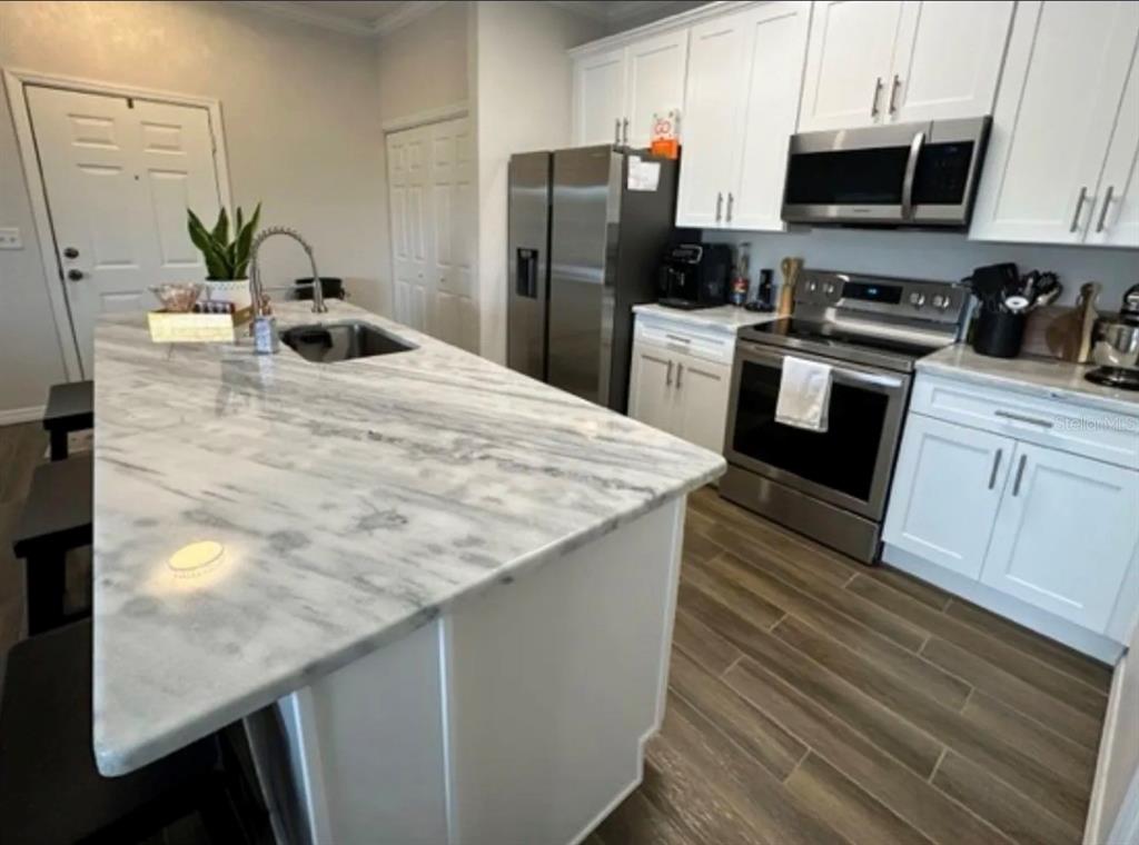 A kitchen features white cabinets, stainless steel appliances, and a large marble-topped island — 306 EAGLE POND DRIVE, WINTER HAVEN, FL