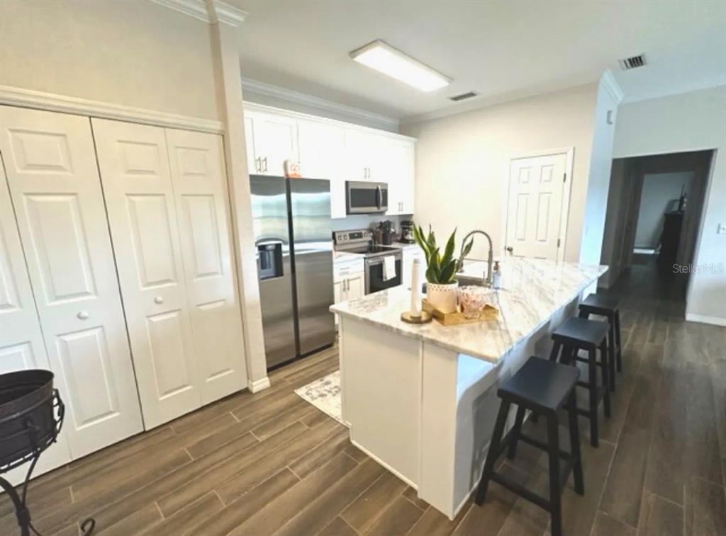 A kitchen features white cabinetry, stainless steel appliances, a marble-topped island, and wood-look tile flooring — 306 EAGLE POND DRIVE, WINTER HAVEN, FL