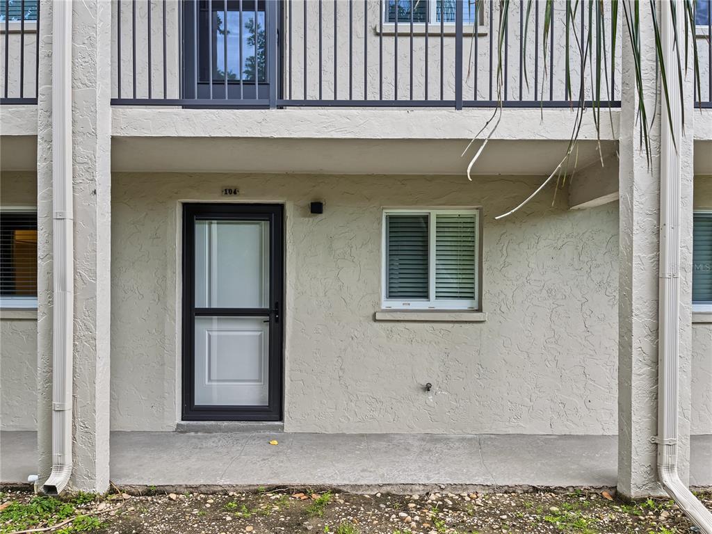 The exterior of a ground-floor apartment unit features a front door, window, and concrete patio — 6470 HOLLYWOOD BOULEVARD UNIT 104, SARASOTA, FL