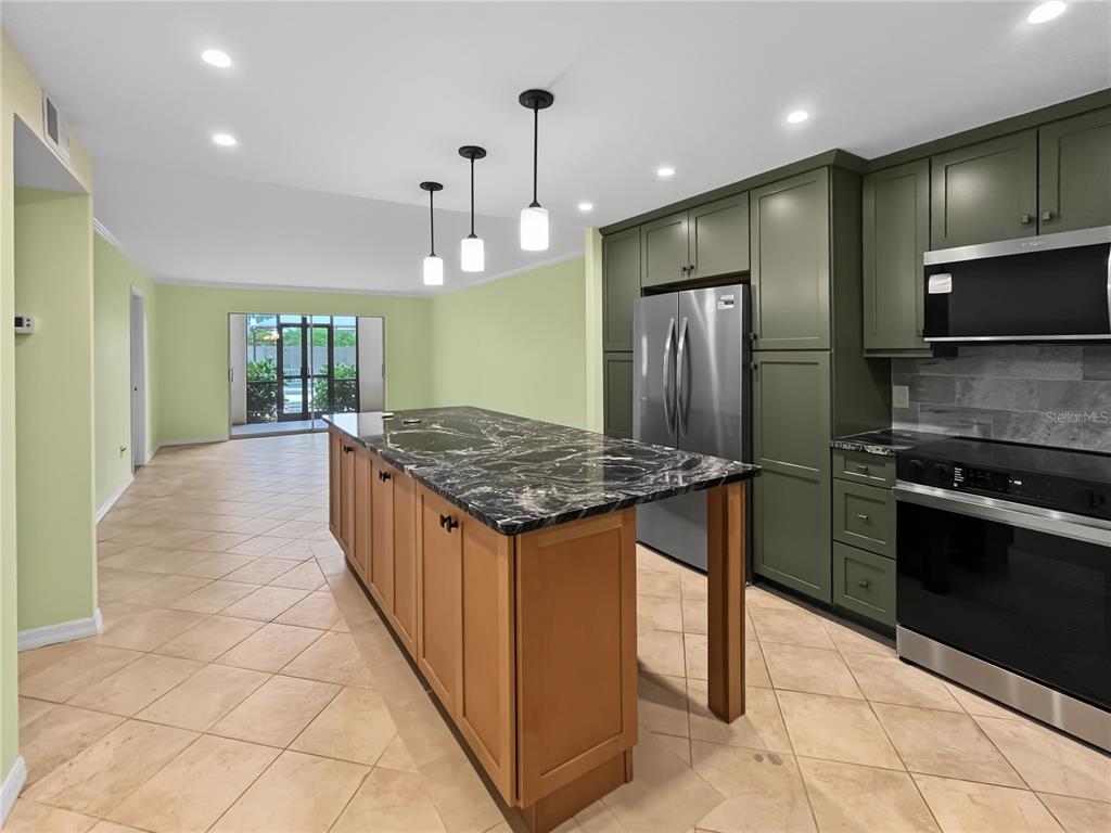 A kitchen features a black marble island, olive green cabinets, and light-colored tile flooring — 6470 HOLLYWOOD BOULEVARD UNIT 104, SARASOTA, FL