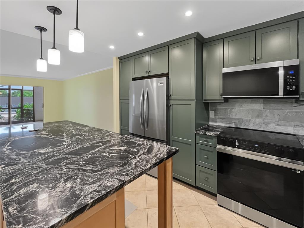 A kitchen features green cabinets, a black marble island, stainless steel appliances, and tile flooring — 6470 HOLLYWOOD BOULEVARD UNIT 104, SARASOTA, FL
