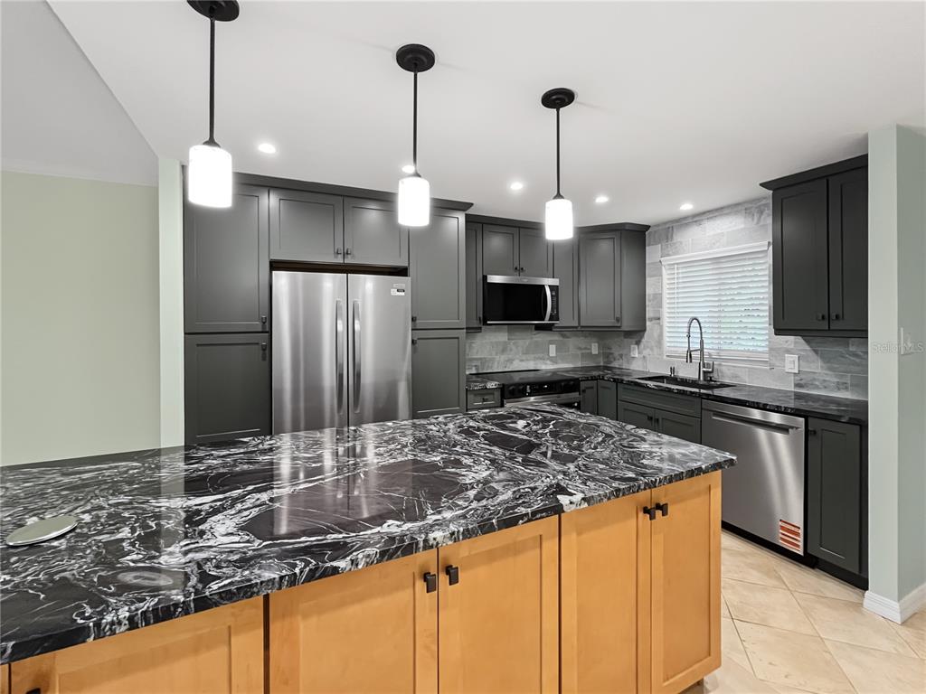 A kitchen features dark gray cabinets, a light wood island, and black and white marble countertops — 6470 HOLLYWOOD BOULEVARD UNIT 104, SARASOTA, FL