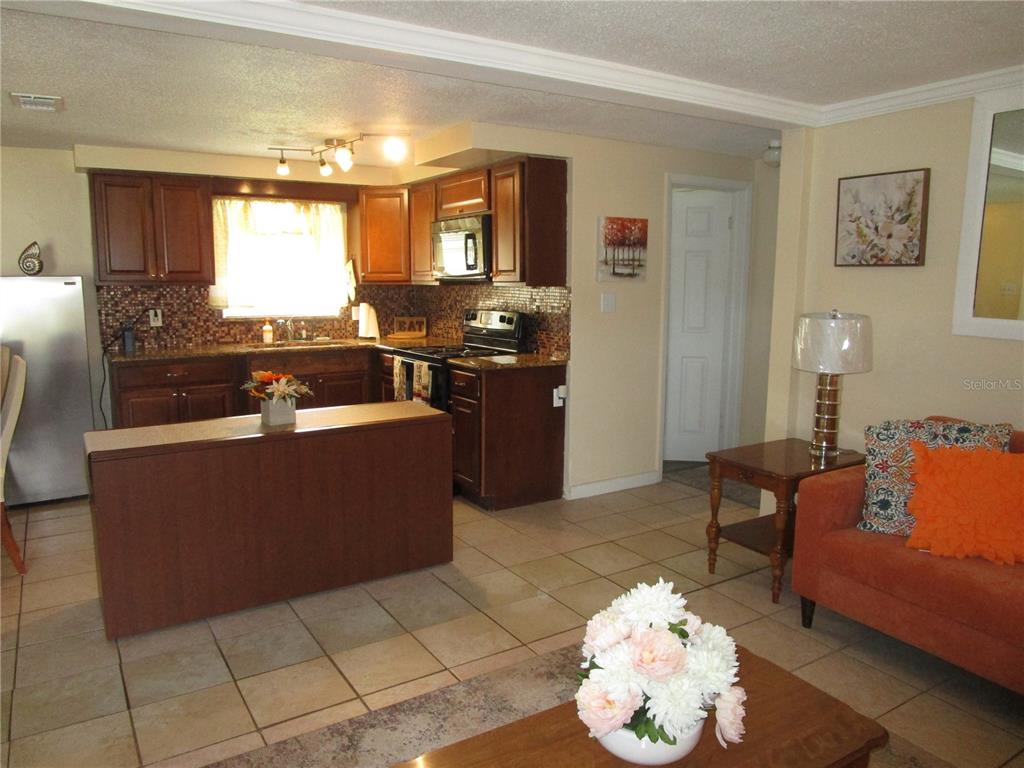 A kitchen with dark wood cabinets and tile flooring opens into a living area — 10801 FILLMORE AVENUE, PORT RICHEY, FL