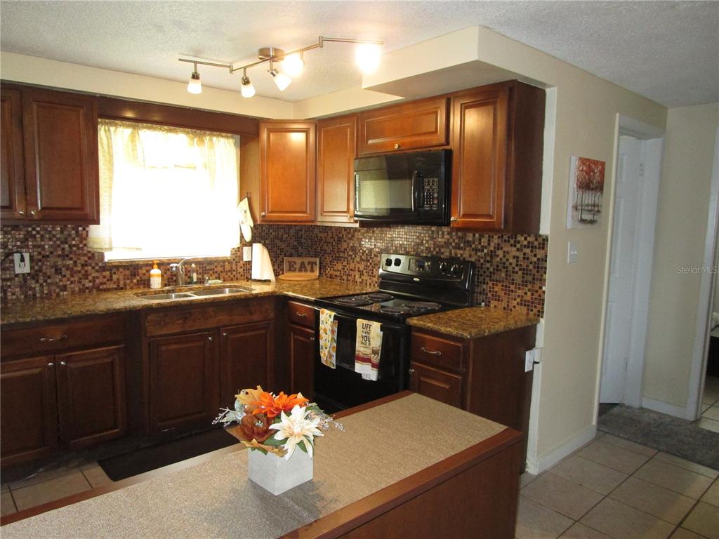 A kitchen with wood cabinets, granite countertops, a mosaic tile backsplash, and a center island — 10801 FILLMORE AVENUE, PORT RICHEY, FL