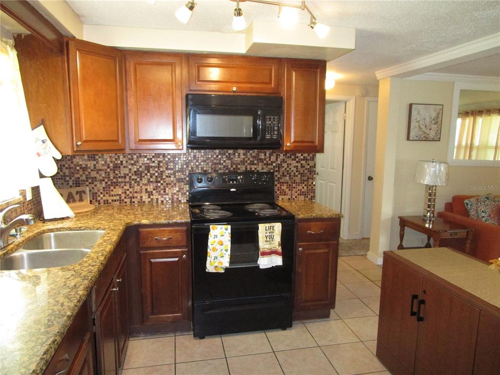 A kitchen with wood cabinets, granite countertops, a mosaic backsplash, and black appliances — 10801 FILLMORE AVENUE, PORT RICHEY, FL