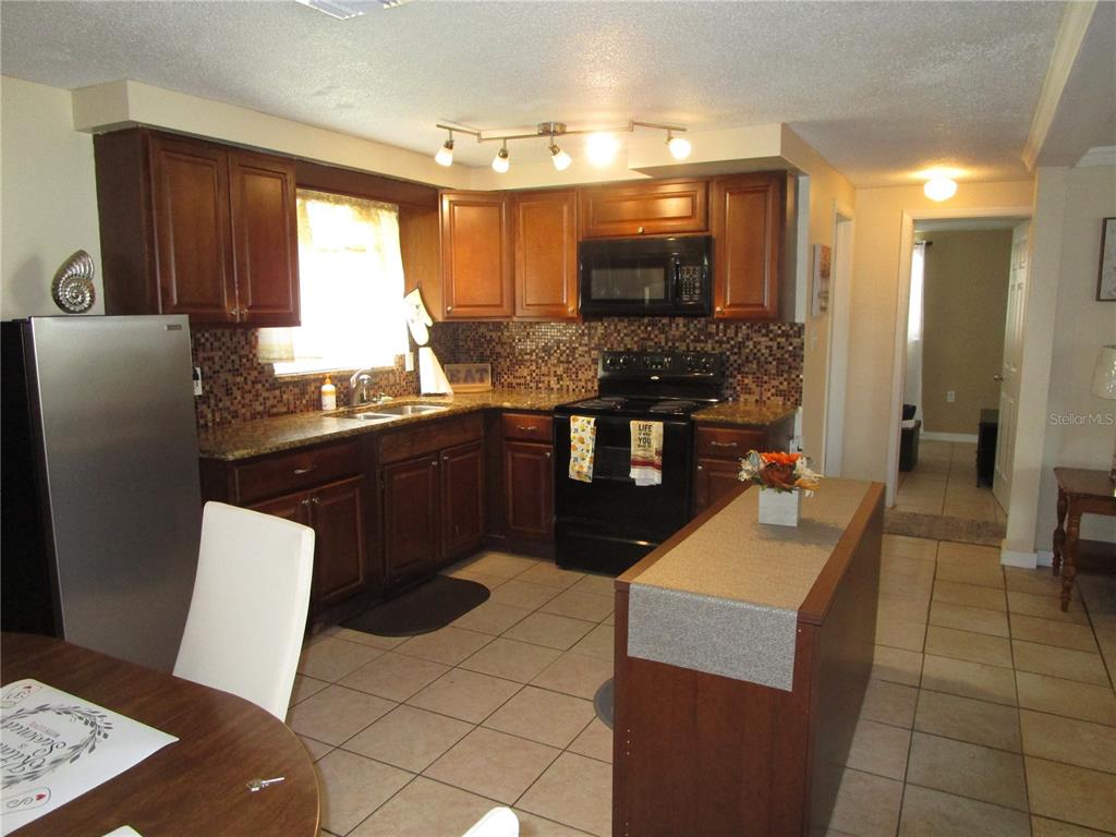 A kitchen with dark wood cabinets, granite countertops, a mosaic backsplash, and a center island — 10801 FILLMORE AVENUE, PORT RICHEY, FL