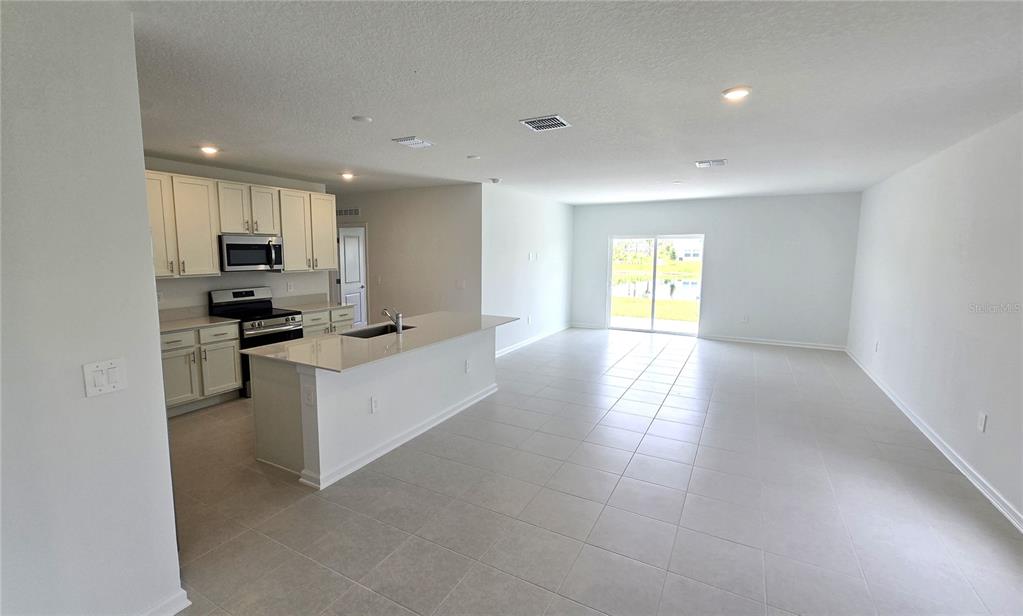 An open-concept kitchen with white cabinets and a large island overlooks a tiled living area — 5618 GINGHAM DRIVE, KISSIMMEE, FL