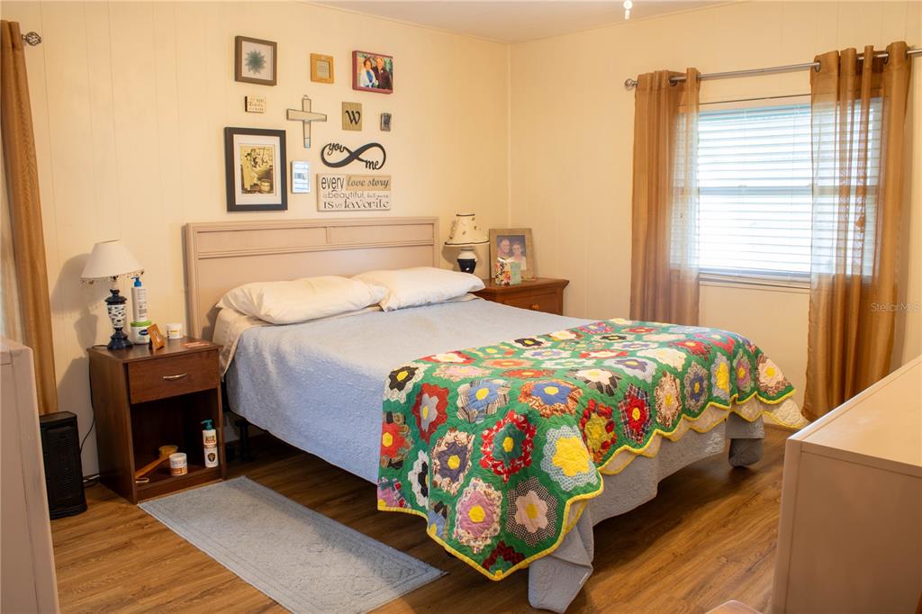 A bedroom features a bed with a colorful quilt, wood-look flooring, and a window with curtains — 4332 CHERRYWOOD STREET, WINTER HAVEN, FL