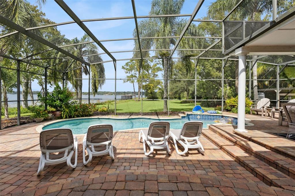 A screened-in patio features a swimming pool, lounge chairs, and a view of a lake — 7051 SADLER ROAD, MOUNT DORA, FL
