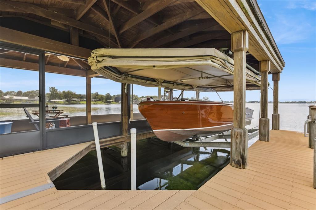 A wooden boat sits on a lift under a covered dock overlooking a lake — 7051 SADLER ROAD, MOUNT DORA, FL
