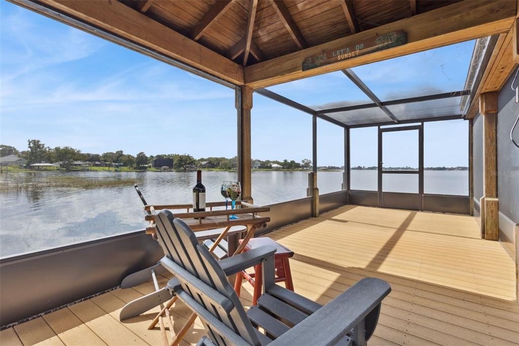 A screened-in wooden deck overlooks a lake with two chairs and a small table — 7051 SADLER ROAD, MOUNT DORA, FL