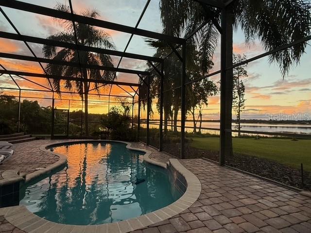 A swimming pool inside a screened-in lanai overlooks a lake at sunset — 7051 SADLER ROAD, MOUNT DORA, FL