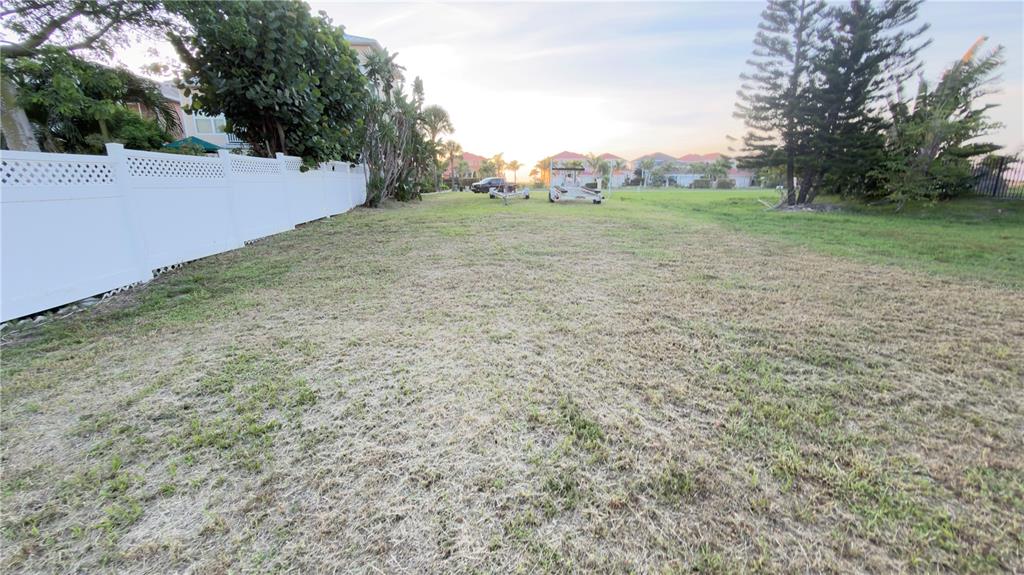 A grassy vacant lot is bordered by a white vinyl fence and mature trees — 6435 MARBELLA BOULEVARD, APOLLO BEACH, FL