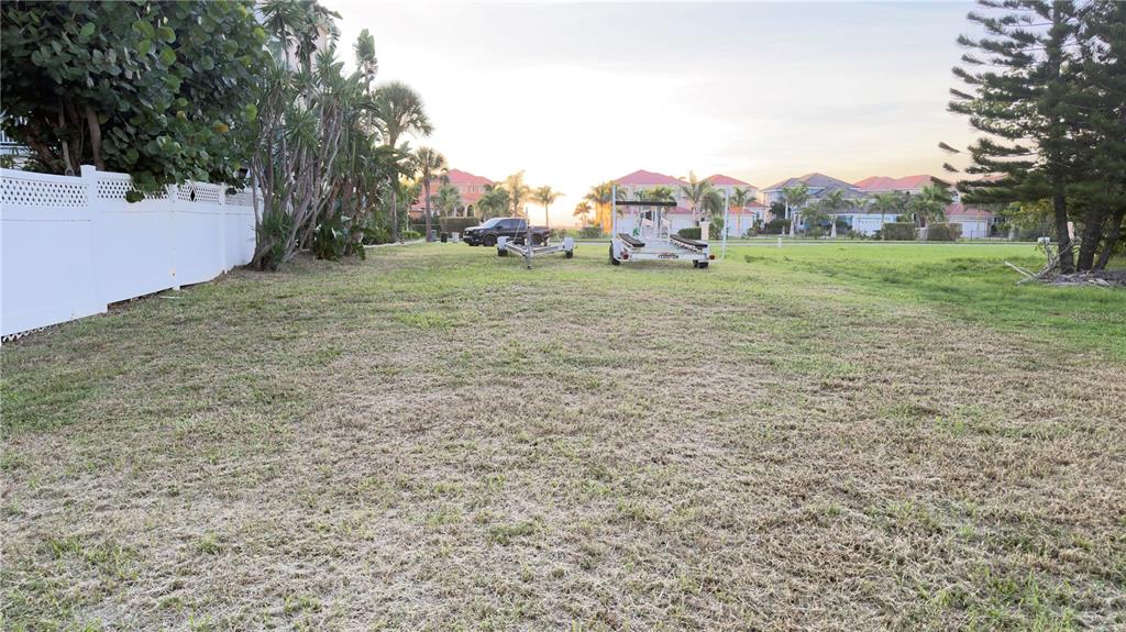 A grassy vacant lot features a white fence, a boat trailer, and distant residential houses — 6435 MARBELLA BOULEVARD, APOLLO BEACH, FL
